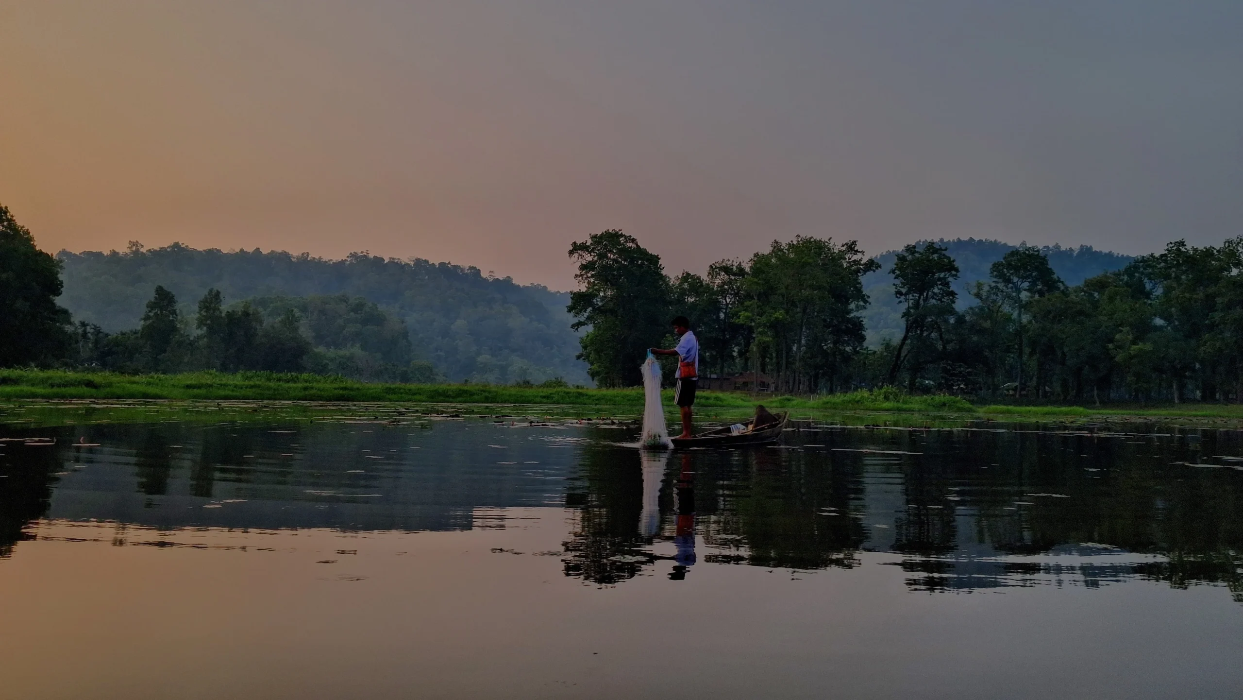 Fisherman spreading a fishing net from a boat on Chandubi Lake at dusk